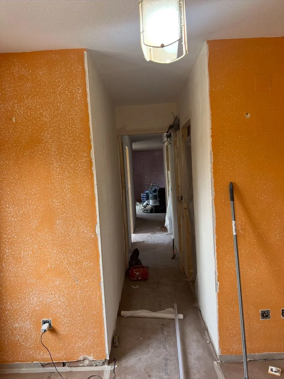 Pasillo con las paredes pintadas de naranja y con gotelé, suelo de obra sin pavimentar y plásticos de protección